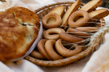 An edible composition of flour baking in a basket on a bedspread, among Golden ears of barley in nature. A big fat donut, vanilla crackers and bagels round