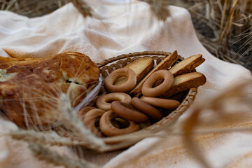 An edible composition of flour baking in a basket on a bedspread, among Golden ears of barley in nature. A big fat donut, vanilla crackers and bagels round