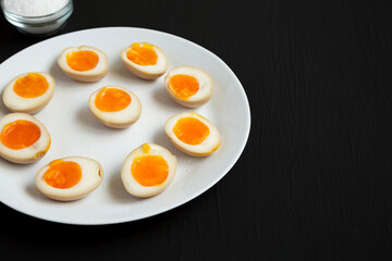 Homemade Unami Soy Sauce Eggs on a white plate on a black background, side view. Copy space.