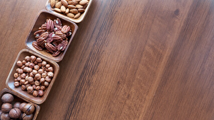 Wooden bowl with mixed nuts on table top view. Healthy food and snack. Walnut, pistachios, almonds, hazelnuts and cashews.