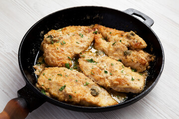 Homemade Italian Chicken Piccata in a cast iron pan on a white wooden background, side view.