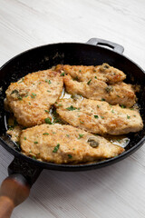 Homemade Italian Chicken Piccata in a cast iron pan on a white wooden table, side view.