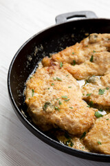 Homemade Italian Chicken Piccata in a cast iron pan on a white wooden background, side view. Close-up.