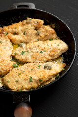 Homemade Italian Chicken Piccata in a cast iron pan on a black background, side view.