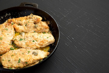 Homemade Italian Chicken Piccata in a cast iron pan on a black background, side view. Copy space.