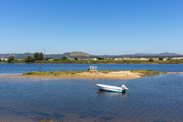 Fototapeta na wymiar Fão / Esposende / Portugal - July 29, 2020: A small boat moored in the Cavado River estuary on a sunny day. Word FAO made of stone concrete letters.