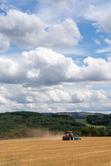 red tractor pulling a blue field cultivator across a harvested wheat field