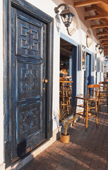 Seafront mediterranean cafe with white walls, beautiful deep blue wooden doors and light blue windows in setting sun. Summer vacation. Travel concept.