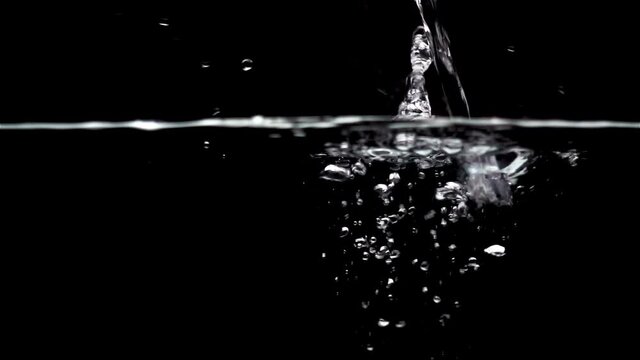 Splashes of water pouring onto the water surface in slow motion on a black background.