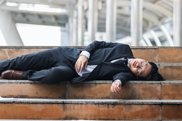 Tired depressed young Asian business man lying down on stairs and suffering from severe depression. Unemployment and layoff concept.