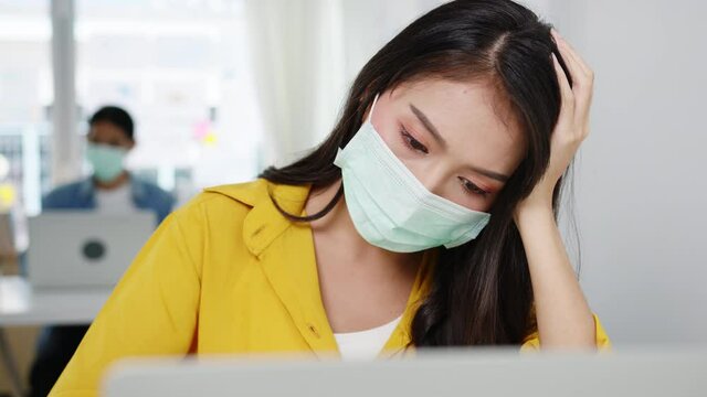 Freelance Asia women wear face mask using laptop hard work at new normal home office. Working from house overload, self isolation, social distancing, quarantine for corona virus prevention.