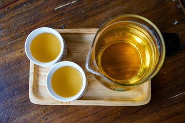 simple still life with green tea, flat lay. Chinese tea in a transparent teapot and two traditional white Asian mugs. On a wooden table and a tray
