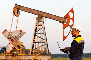 engineer with a laptop on the background of an oil pump