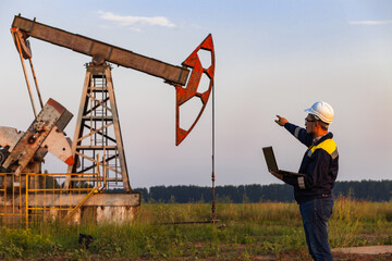 engineer with a laptop on the background of an oil pump