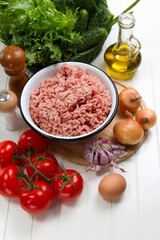 Fresh turkey mince, tomatoes, onions, garlic, herbs, cucumbers, egg, olive oil, salt and pepper on a table