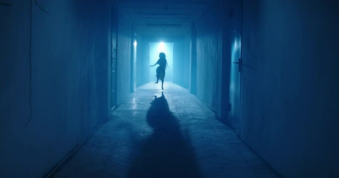 Little girl in white dress looking like a ghost carelessly running down the hallway of a haunted house - halloween costume party, horror movie 4k footage