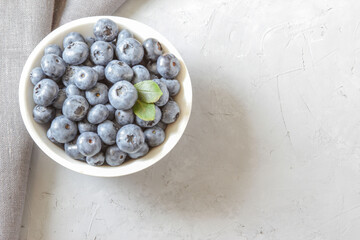Fresh blueberries in white bowl. Fresh blueberries with green leaves on gray table. Concept for healthy eating and nutrition. Top view. Copy space.