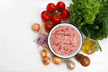 Fresh turkey mince, tomatoes, onions, garlic, herbs, cucumbers, egg, olive oil, salt and pepper on a table