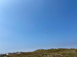 Fototapeta na wymiar Paraglider in the blue sky. The sportsman flying on a paraglider in Esposende, Portugal.
