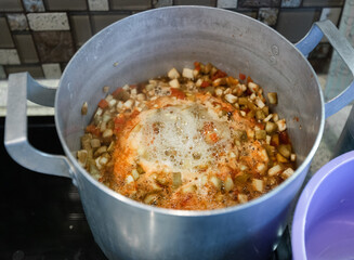A large stock pot on a stove with vegetables cut for making vegetable stew. Boiling vegetables in water. Homemade food.
