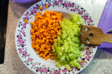 Plate with chopped  frying carrots and green pepers  as ingredients for vegetable stew.Top view. Spatula, cutting board, bowl.
