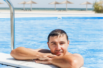Young handsome man enjoying summer vacation in a luxurious pool. Young European man relaxes in the pool at the resort. Relaxation concept. Guy in the outdoor pool at a luxury hotel.