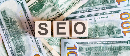 Concept words SEO on wooden blocks on a beautiful background from dollar bills.