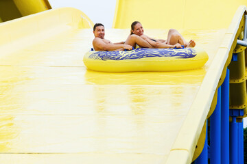 A man and a woman ride a large slide in the water park. Family vacation at the water park. Entertainment and attractions in the water park. Happy family couple vacation.