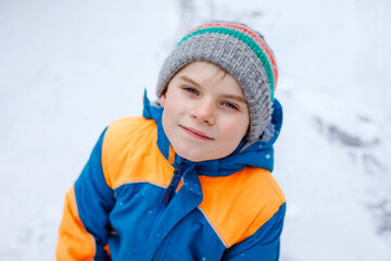 Portrait of little school kid boy in colorful clothes playing outdoors during snowfall. Active leisure with children in winter on cold snowy days. Happy healthy child having fun and playing with snow.