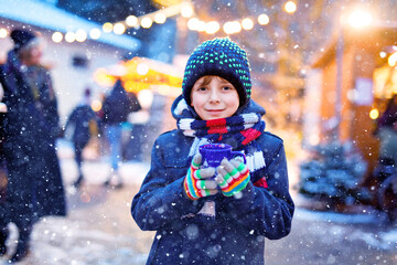 Little cute kid boy drinking hot children punch or chocolate on German Christmas market. Happy child on traditional family market in Germany, Laughing boy in colorful winter clothes