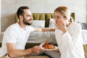 Optimistic loving couple eating croissants