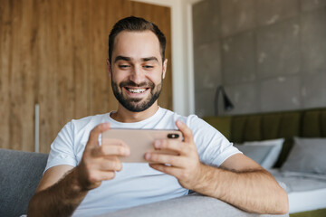 Image of joyful handsome man playing video game on cellphone © Drobot Dean