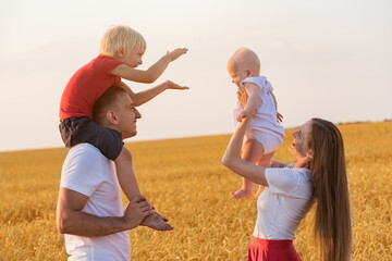 Cheerful young family outdoors. Mom, dad and two kids having fun in wheat field.
