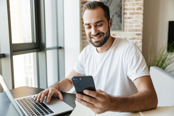 Image of man working with laptop and cellphone while sitting at table