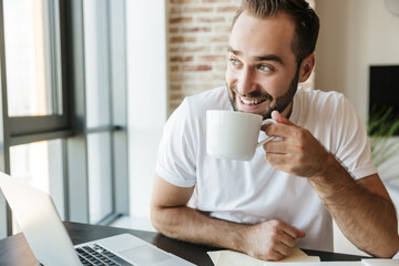 Fototapeta na wymiar Image of man drinking coffee and using laptop while sitting at table