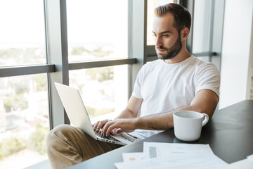 Image of young man working with laptop while sitting at table