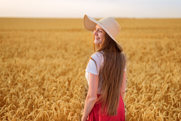 Obraz premium Beautiful young woman in hat walking on field of ripe wheat