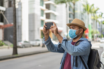 Young asian backpacker traveling in urban city and take the photo. He wearing face mask for protect virus safety travel.