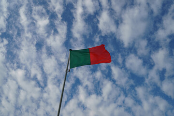 Photography of Portugal flag. Blue sky with white fine clouds as background.