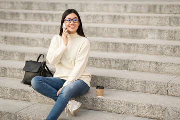 Young female student using phone, sitting on stairs