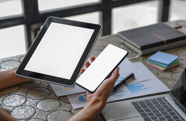 Close-up shot of a Mockup blank screen tablet and  smartphone in woman hand and a laptop on the desk.