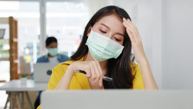 Freelance Asia women wear face mask using laptop hard work at new normal home office. Working from house overload, self isolation, social distancing, quarantine for corona virus prevention.