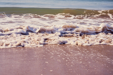 Sandy beach on a sunset with reflection on wet sand and waves with foam. Copy space. 