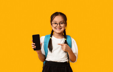Asian Schoolgirl Showing Smartphone Empty Screen Over Yellow Studio Background