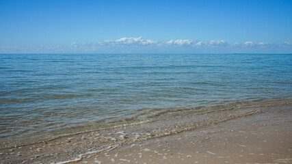  Blue sea with Gentle wave breaking on the sand and clouds on the horizon.
