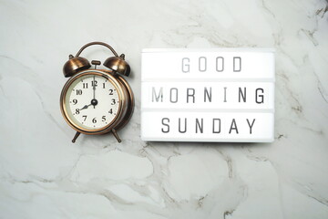 Good Morning Sunday word in light box and alarm clock Flat lay