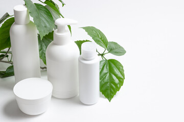 Set of cosmetic cans of organic cosmetics for face and body care on a white background with green leaves. Cream, shampoo and lotion on a light background. Layout, copy space.