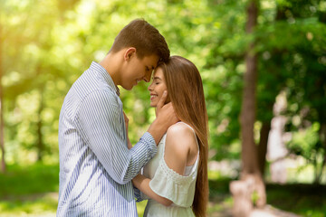 Fototapeta premium Romantic relationship. Handsome young guy and his girlfriend cuddling in park on summer day