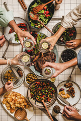 Summer barbeque party. Flat-lay of table with grilled meat, vegetables, salad, roasted potato and peoples hands feasting over checkered tablecloth, top view. Family gathering, comfort food concept