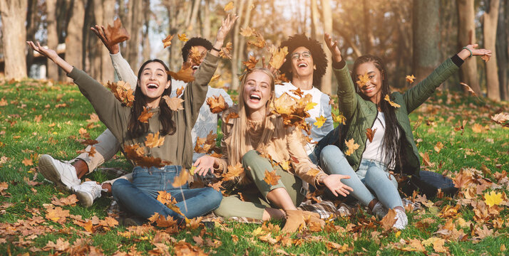 Carefree young friends taking photos with autumn leaves in park